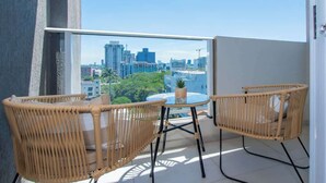 A balcony with wicker chairs and a small table, overlooking a cityscape. - Corporate Stays First Living - 403 (Asunción)