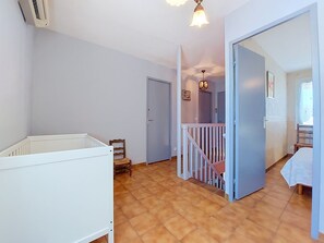 A room with a crib, a wooden chair, a staircase, and a door leading to another room. - L Escapade Orangeoise by Interhome (Orange)
