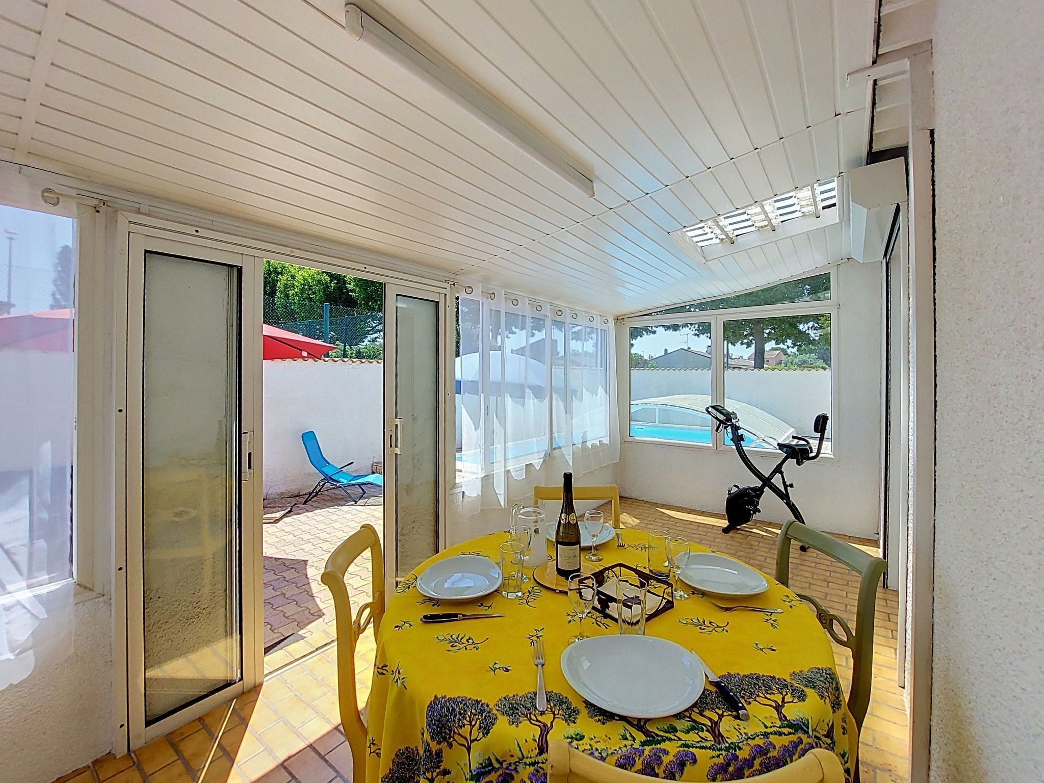 A dining area with a table set for two, a bicycle, and a view of a swimming pool.