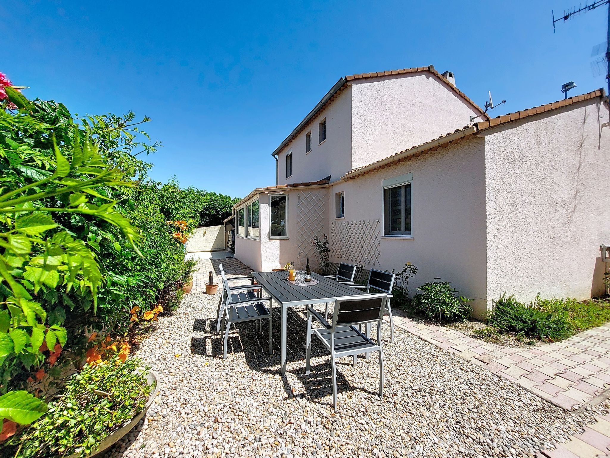 Una casa con patio que incluye una mesa y sillas, rodeado de grava y plantas.