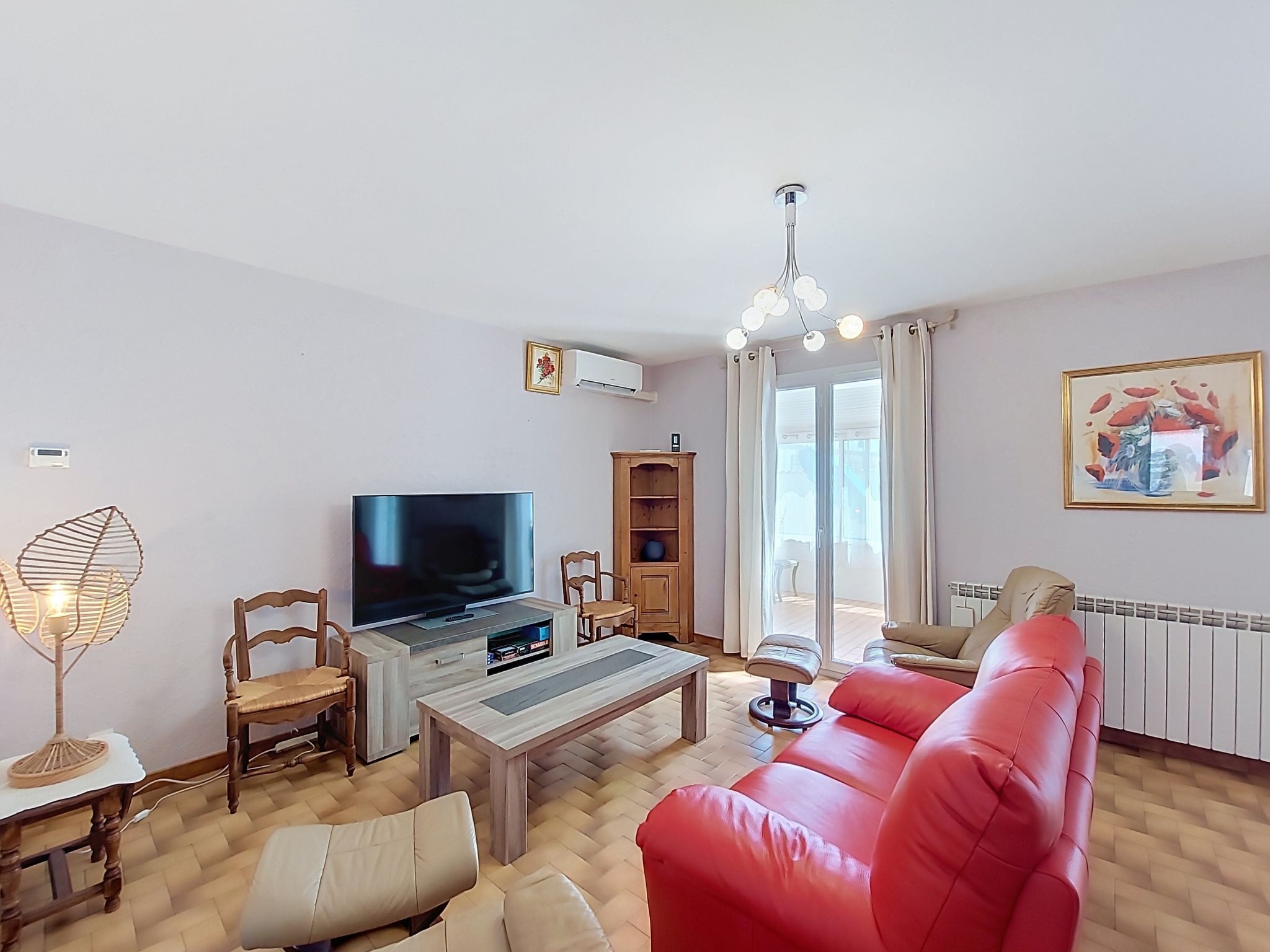 Uma sala de estar com televisão, sofá, mesa de centro, luminária e uma janela com cortinas.