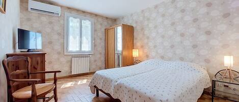 A bedroom with a bed, a chair, a desk, a wardrobe, and a window.