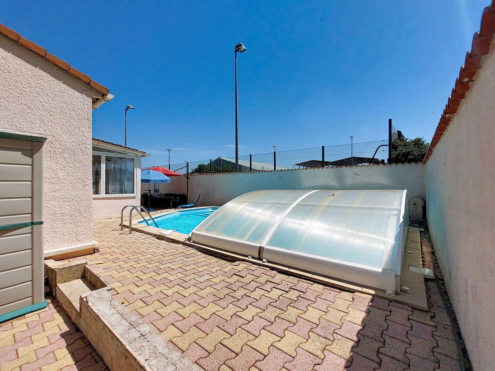 Piscina com estrutura de vidro, rodeada por um espaço de pátio pavimentado.