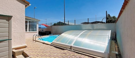 Une piscine dotée d’une enceinte en verre, entourée d’une terrasse dallée.