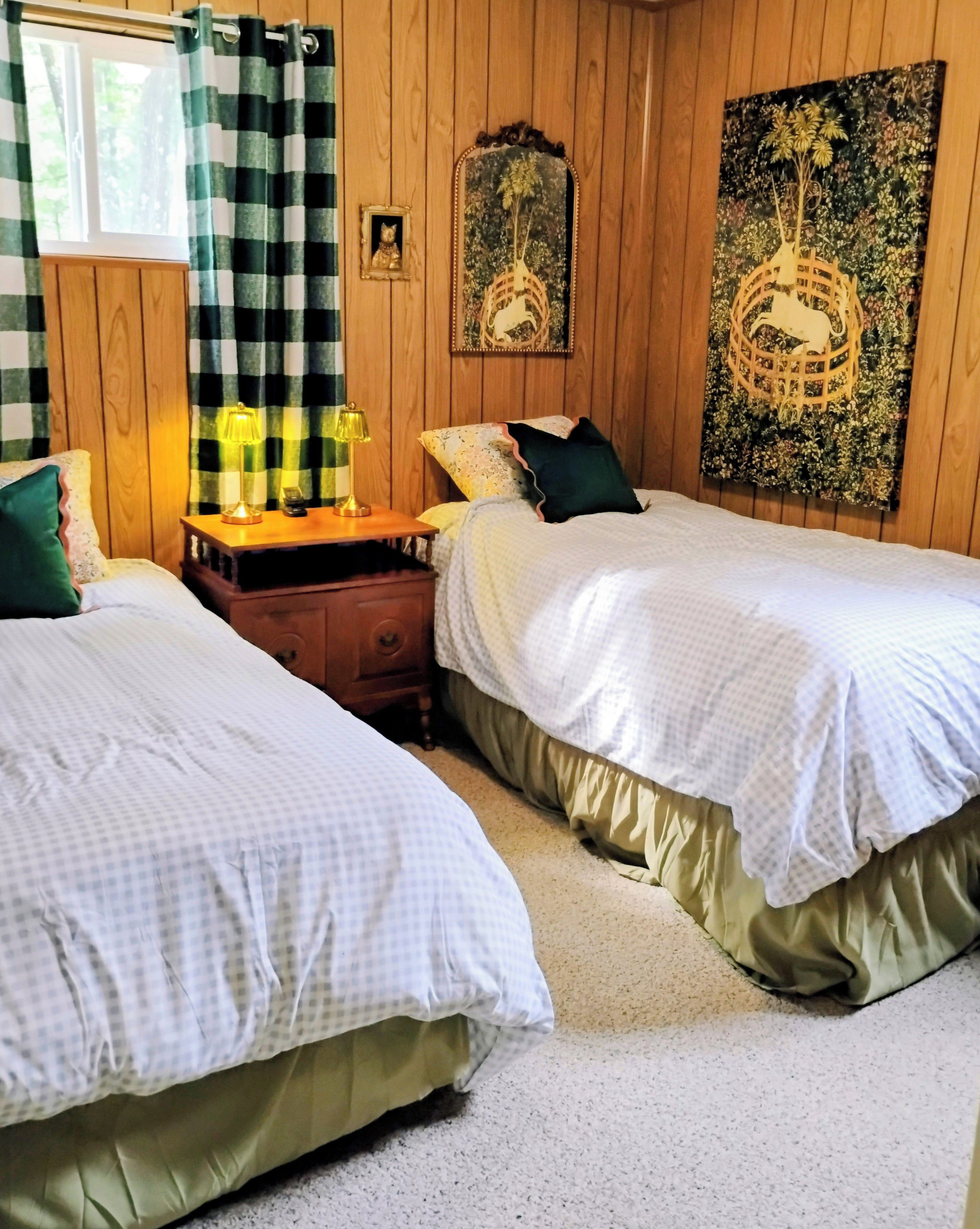 Un dormitorio con dos camas, una mesita de noche, una lámpara y una pared con un espejo decorativo y obras de arte.