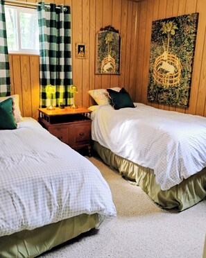Ein Schlafzimmer mit zwei Betten, einem Nachttisch, einer Lampe und einer Wand mit einem Zier-Spiegel und Kunstwerken.