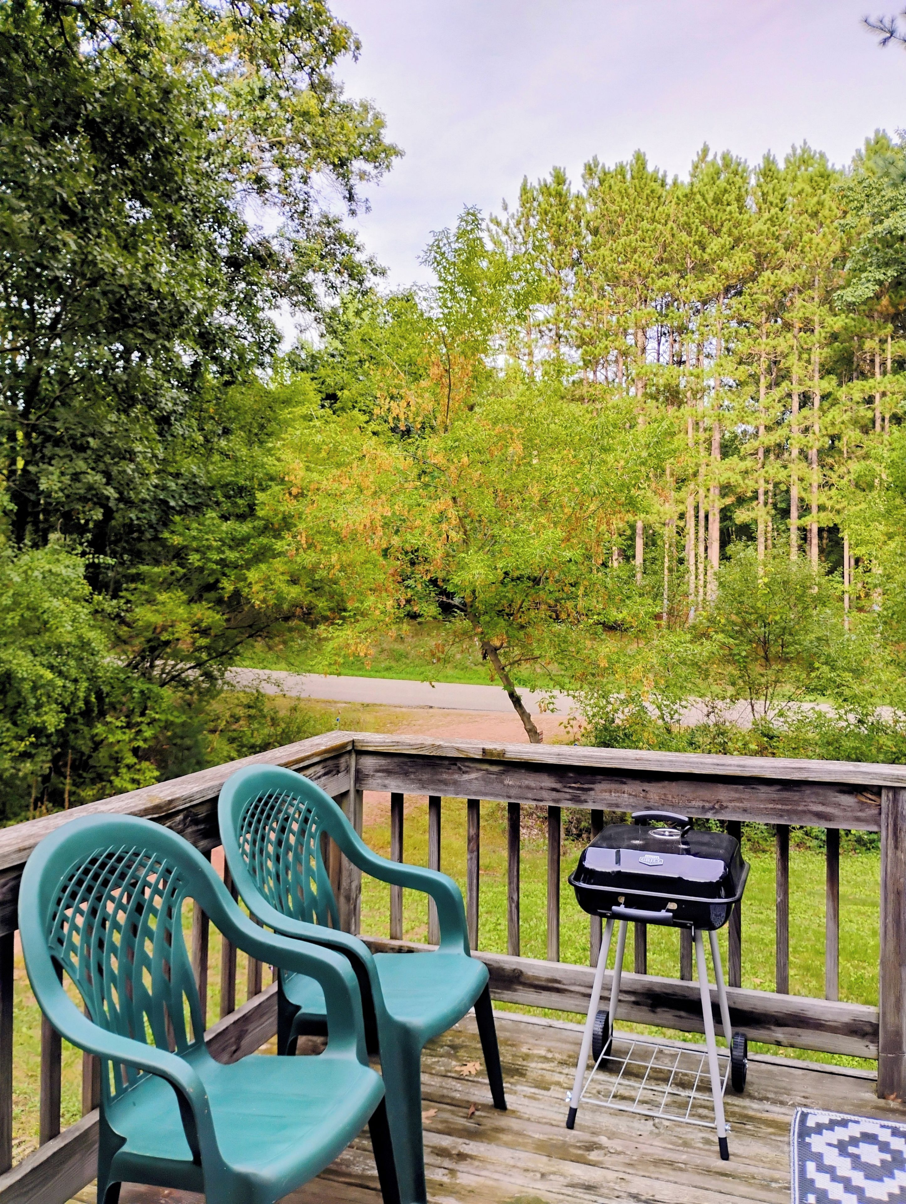 A wooden deck with two green plastic chairs and a grill.