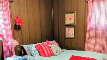 Quarto com cama, mesa de cabeceira, abajur e tapete estampado.