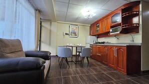 A compact living space with a sofa, a dining table with chairs, a kitchenette with wooden cabinets, and a ceiling light fixture. - Detached House Near Downtown on the Second Floor - Los Profesionales (Cusco)