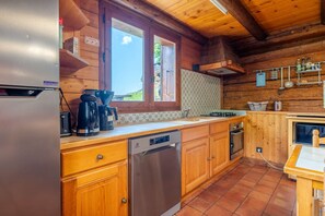 A wooden cabin kitchen with a refrigerator, coffee maker, dishwasher, and a window with a view of the outdoors. - Ravoux : Chalet, terrasse  et  vue montagne (LA CLUSAZ)