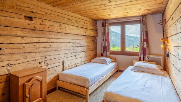 Een houten kamer met twee bedden, een houten kast en een raam met gordijnen.