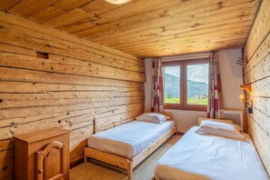 A wooden cabin room with two beds, a wooden cabinet, and a window with curtains. - Ravoux : Chalet, terrasse  et  vue montagne (LA CLUSAZ)