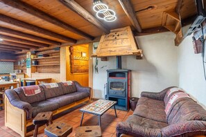 A rustic cabin interior with a wooden ceiling, a sofa, a table, and a wood-burning stove. - Ravoux : Chalet, terrasse  et  vue montagne (LA CLUSAZ)