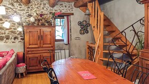 Un intérieur rustique avec une table à manger en bois, des chaises, un buffet, un escalier et un mur en pierre.