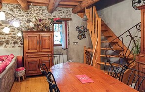 Ein rustikales Interieur mit einem Holzespeisetisch, Stühlen, einem Schrank, einer Treppe und einer Steinwand.