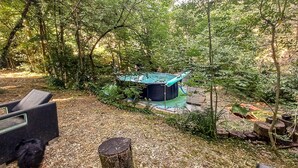 Une zone boisée comprenant une petite structure fermée, qui pourrait être un jacuzzi, entourée d’arbres et recouverte d’une végétation naturelle.