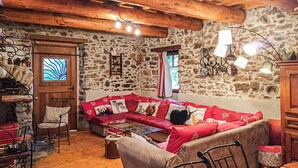 Une pièce chaleureuse avec un mur en pierre, des poutres en bois au plafond, un canapé rouge agrémenté de coussins à motifs animaliers, une table en bois et une chaise.