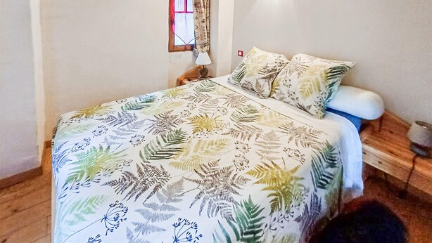 Un lit avec une couvre-lit à motifs floraux, une lampe de chevet et une fenêtre avec des rideaux.