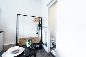 A compact room with a black metal frame bed, a white toilet, a small table with a bowl and a knife, and a wicker basket. - The Bay Apart-Hotel by Guestz (Morecambe)