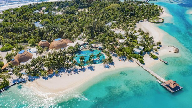 Vista aérea de un resort tropical con playa, palmeras y una piscina.