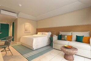 A hotel room with a bed, a sofa, a chair, a small table with fruit, and a patterned rug. - Kandooma Maldives - All Inclusive with Kids Stay & Eat Free (Kandooma)