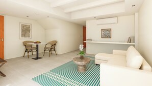 Un salón moderno con un sofá blanco, una mesa de comedor con sillas de mimbre, una mesita redonda con un jarrón de flores y una alfombra estampada.