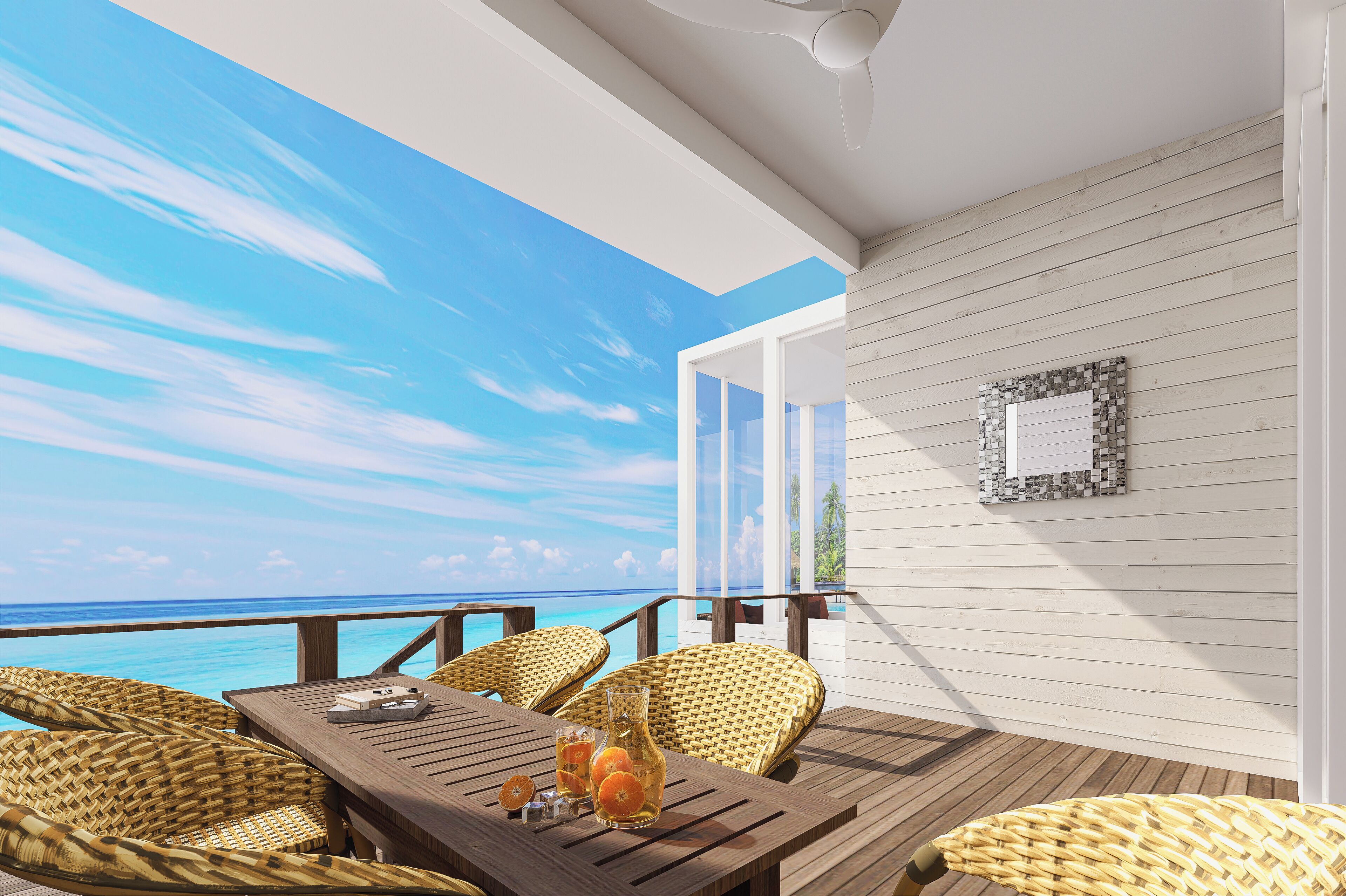 Una terraza de madera con mobiliario de mimbre, una mesa de cristal y vistas al océano.