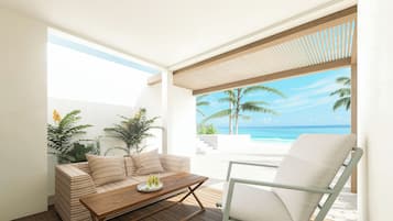 Un espacio exterior moderno con una mesa de madera, un sofá acolchado y una silla, con vista a una playa con palmeras y el océano.