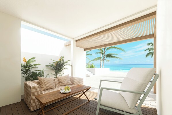 A modern outdoor seating area with a wooden table, a cushioned sofa, and a chair, overlooking a beach with palm trees and the ocean.