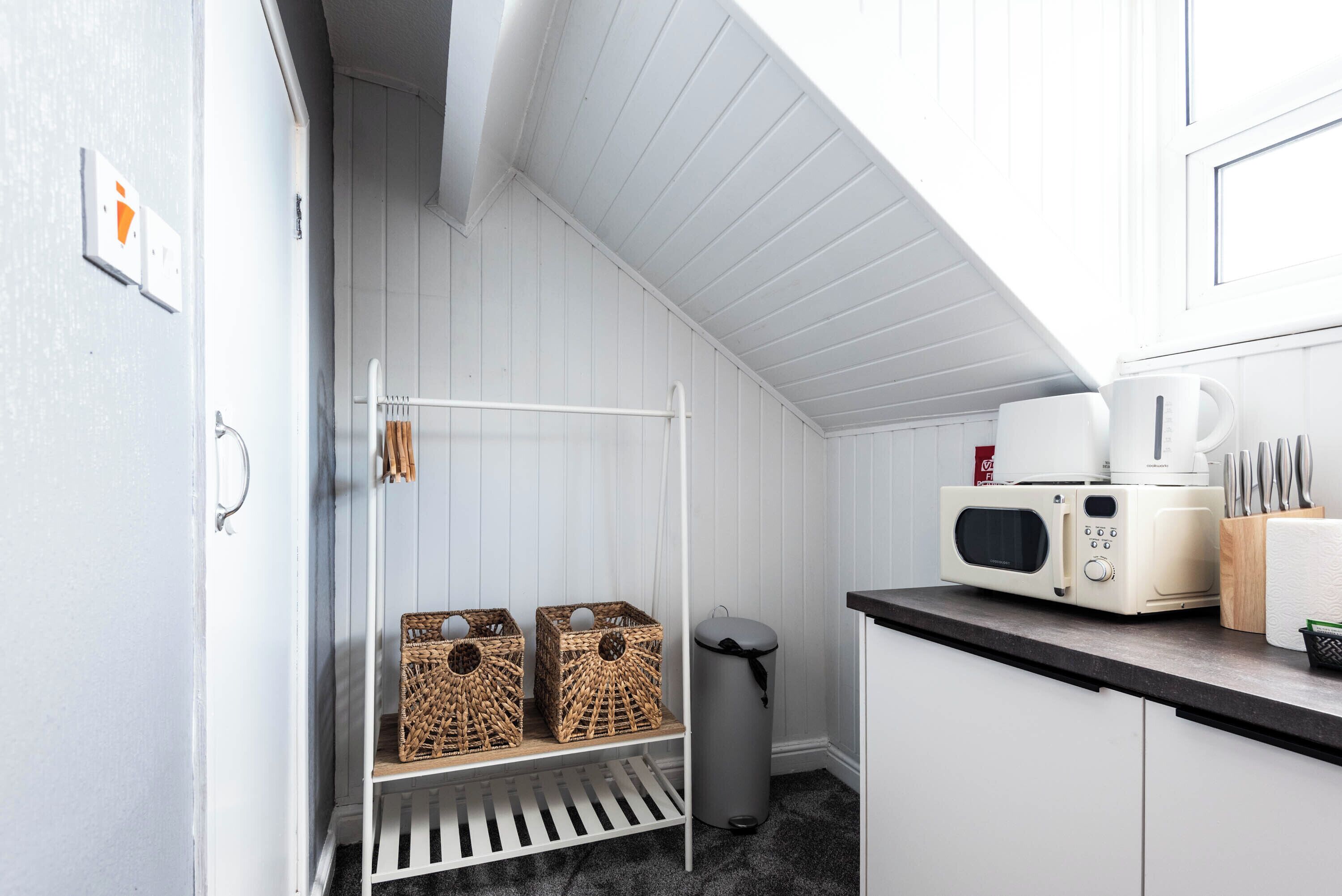 Una cucina con mobili bianchi, un forno a microonde, una macchina da caffè e cesti di vimini su uno scaffale.