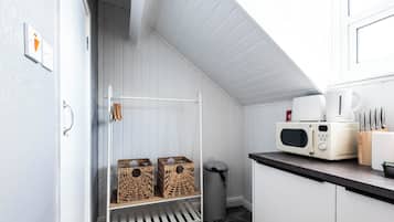 Una cucina con mobili bianchi, un forno a microonde, una macchina da caffè e cesti di vimini su uno scaffale.