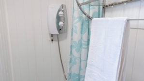 Um chuveiro com parede branca, prateleira de metal e cortina de chuveiro azul com padrão.