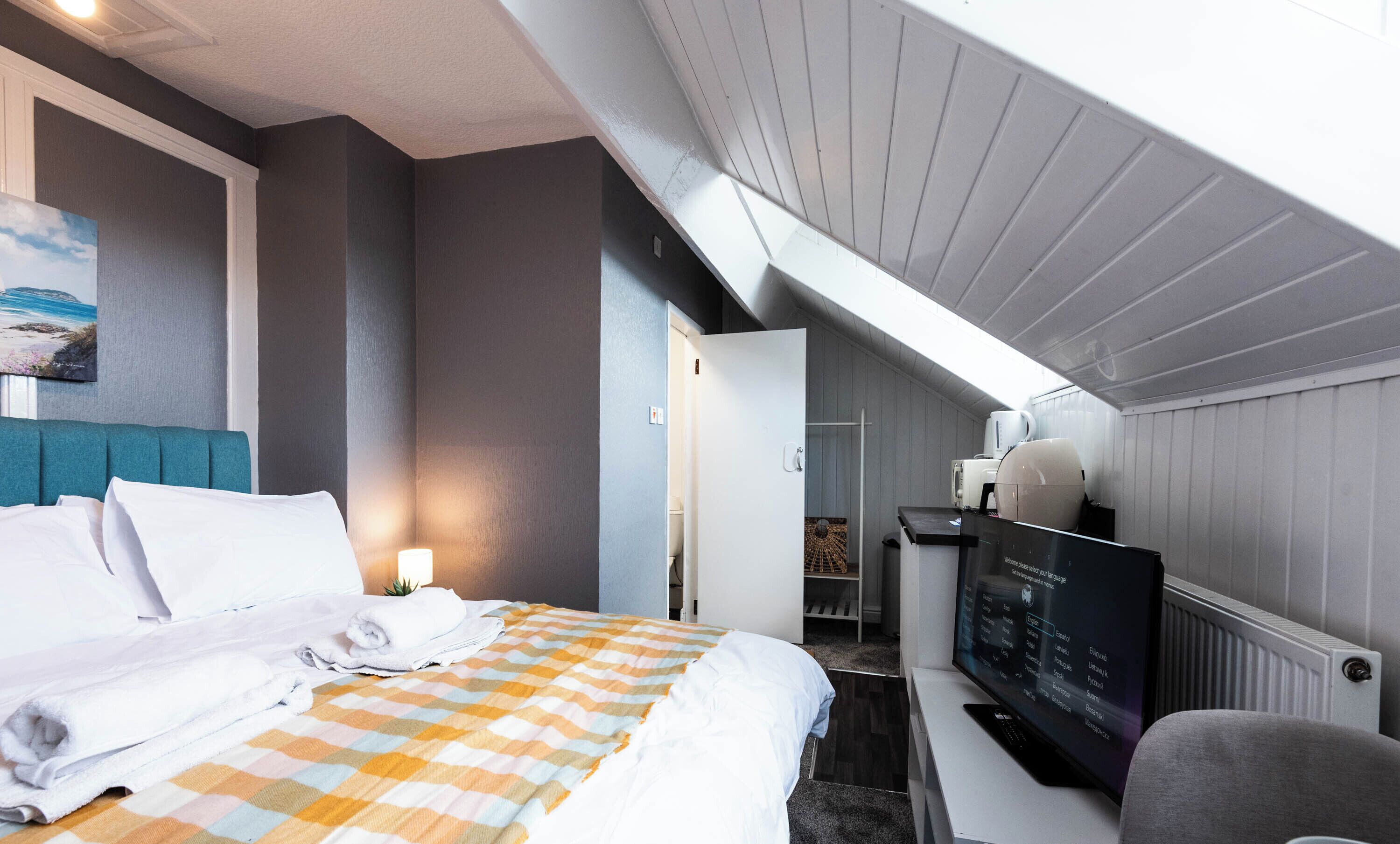 Una habitación de hotel con cama, televisión y baño visible a través de una puerta abierta.