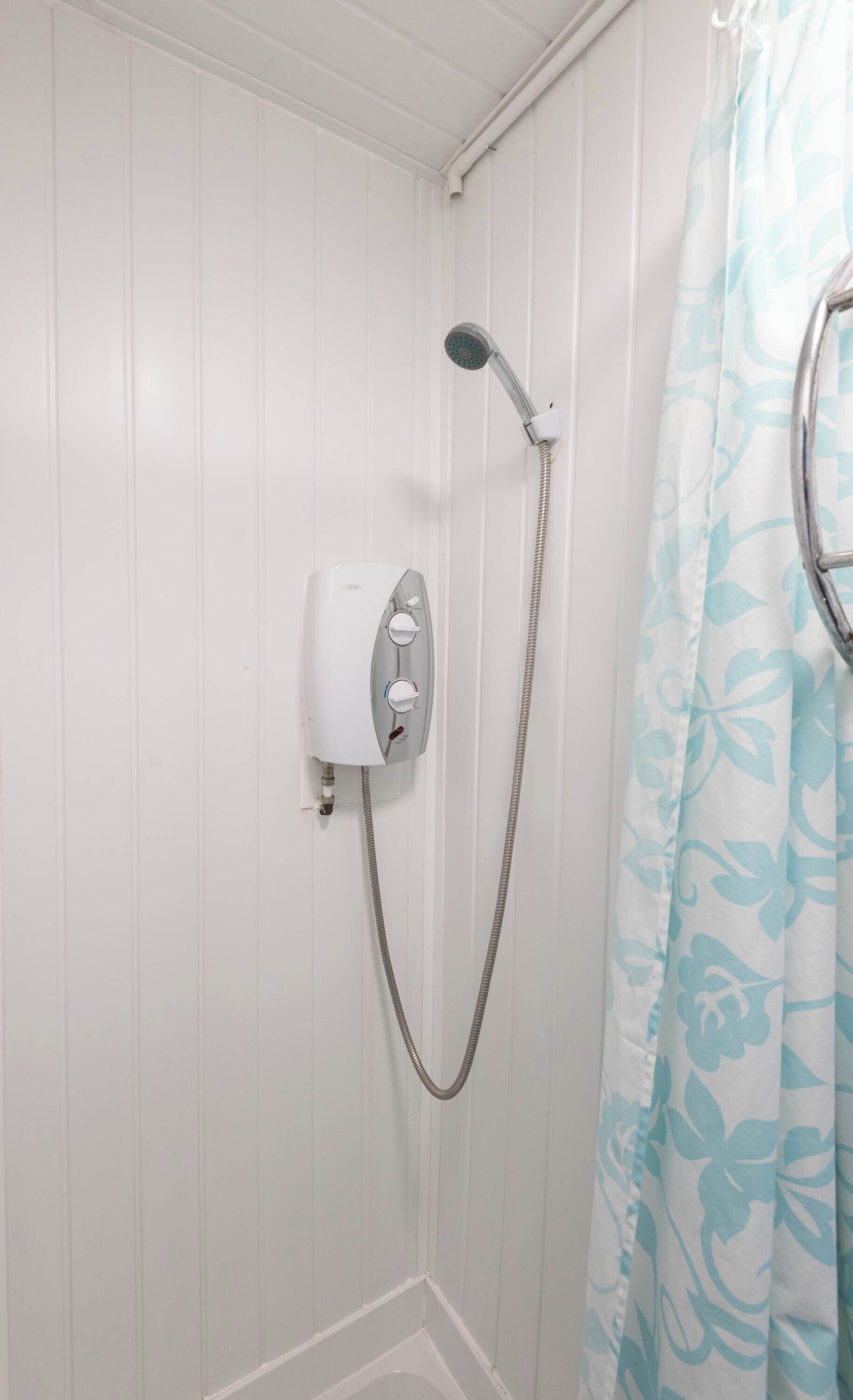 Una ducha con cabezal de ducha de mano y panel de control en la pared.