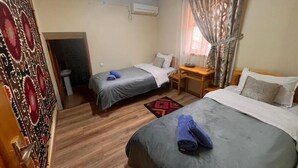 Une chambre d’hôtel avec deux lits, un bureau, une chaise, une petite table, un appareil de climatisation et une porte à motifs.