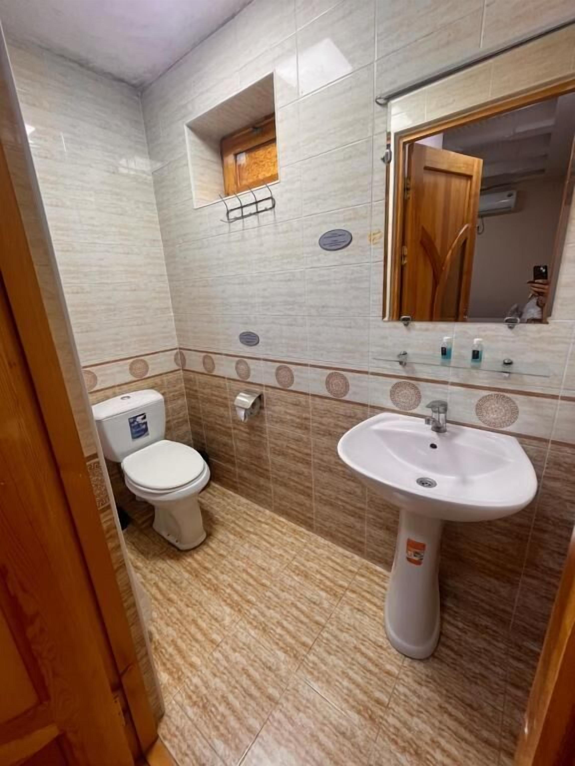 Un baño con inodoro, lavamanos, espejo y paredes con azulejos.