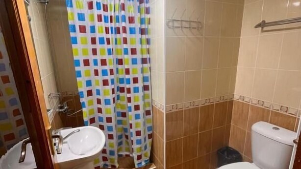 Une salle de bain avec douche, toilettes, lavabo et murs carrelés.