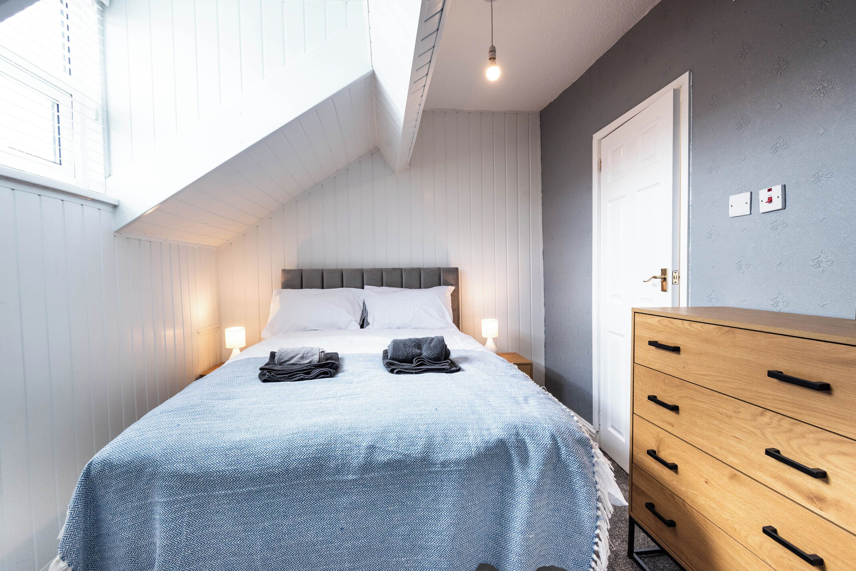 A bedroom with a bed, bedside lamps, a dresser, and a door.