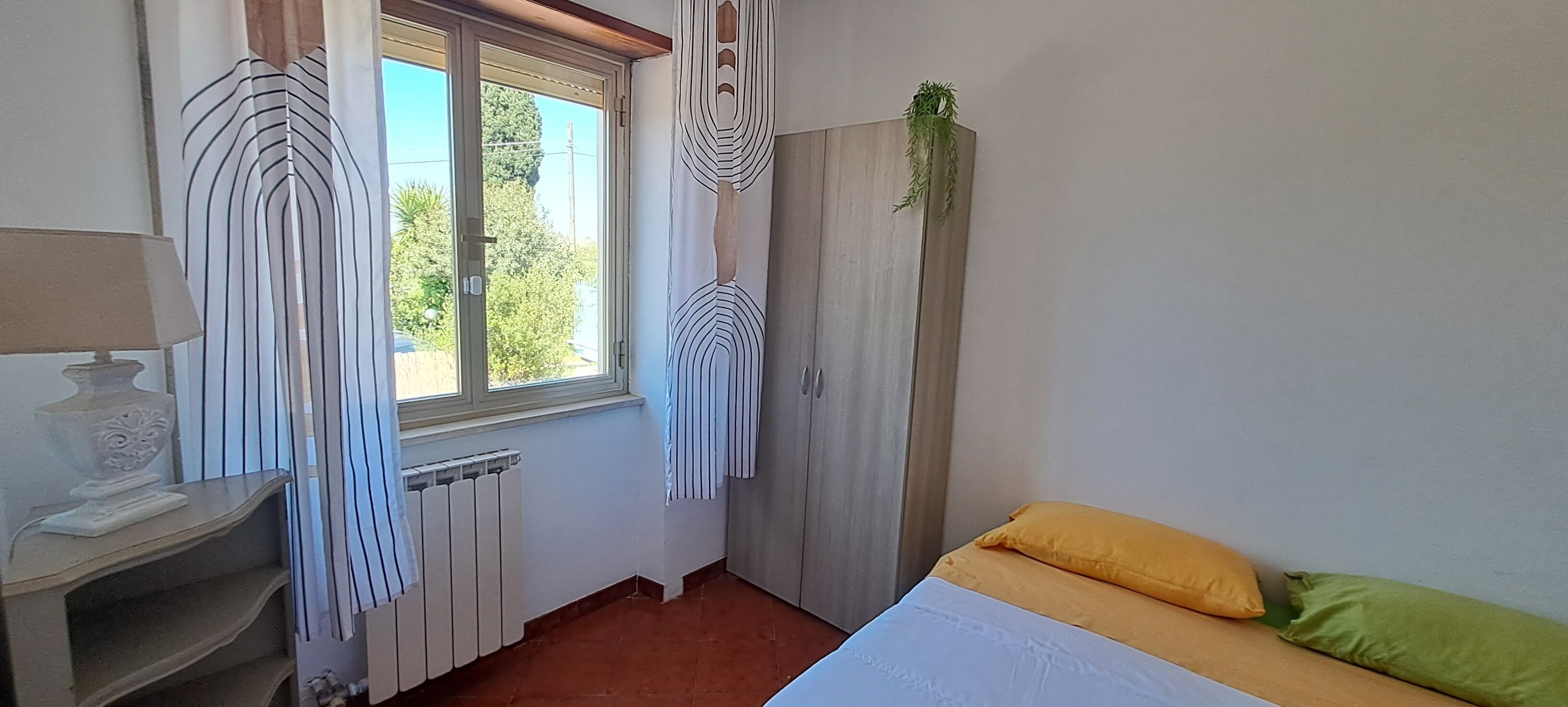 A bedroom with a bed, a radiator, a window with curtains, and a plant on the wall.