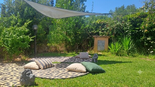 A grassy outdoor area with a patterned mat, pillows, and a statue. - The Rainbow House (Roma)