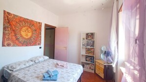 A bedroom with a bed, a tapestry, a bookshelf, and a fan. - The Rainbow House (Roma)