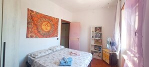 Ein Schlafzimmer mit einem Bett, einer Wandteppich, einem Bücherregal und einem Ventilator.