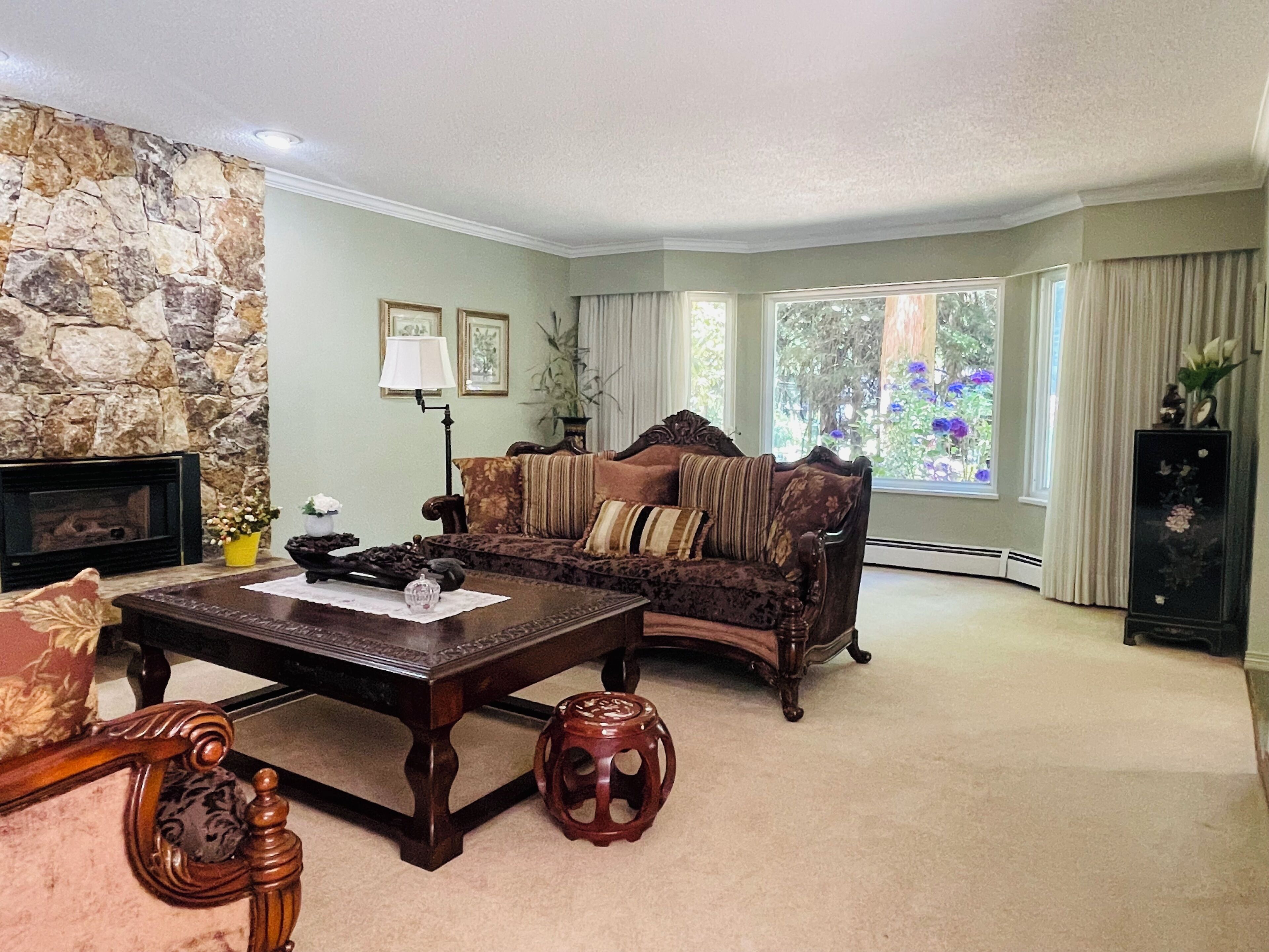A living room with a stone wall, a fireplace, a sofa, a coffee table, and a view of the outdoors.