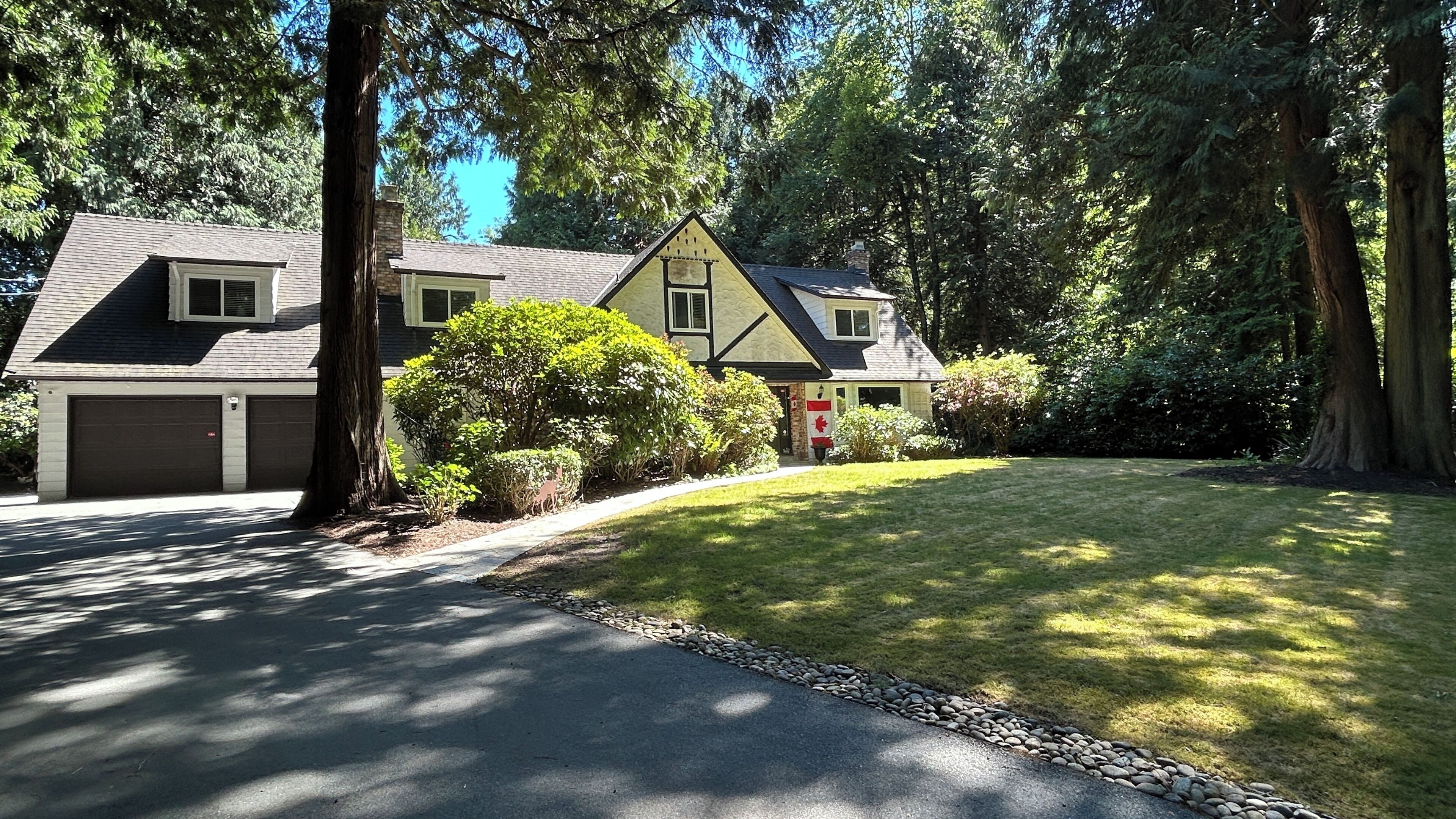 A two-story house with a garage, surrounded by trees and a well-maintained lawn.