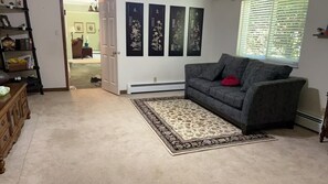 A living room with a grey sofa, a patterned rug, a wooden dresser, and a door leading to another room. - Woodland Manor - Forest Estate Near Crescent Beach (Surrey)