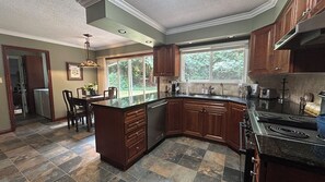 A kitchen with a large island, dark wooden cabinets, a built-in stove, and a window providing a view of the outdoors. - Woodland Manor - Forest Estate Near Crescent Beach (Surrey)