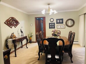 A dining room with a wooden table and chairs, a chandelier, and wall decorations including a clock and framed pictures. - Woodland Manor - Forest Estate Near Crescent Beach (Surrey)