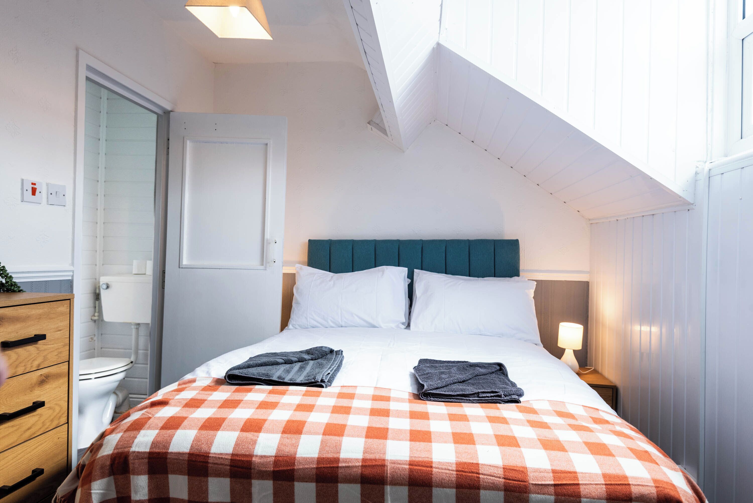 Une chambre d’hôtel avec un lit, une table de chevet, une lampe, une fenêtre et une porte.