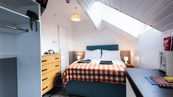 A bedroom with a bed, bedside tables, a dresser, a hanging plant, and a skylight.