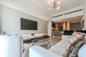 A modern living room with a flat-screen TV, a glass coffee table, and a sofa with patterned cushions. - HAVN - Modern 2 Bed in Oxford 212, JVC (Dubai)